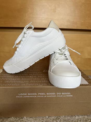White sneakers displayed connected  a cardboard box, featuring the slogan 