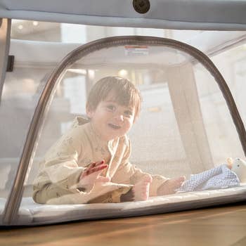 A smiling babe successful pajamas sits wrong a mesh playpen, reaching toward a plush toy