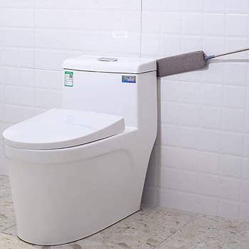 the brush being used to clean a gap between a toilet and a wall