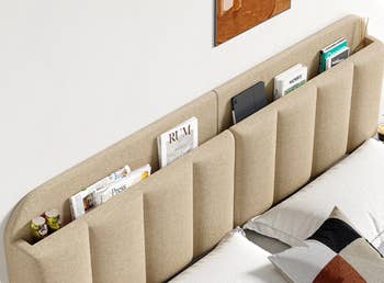 Fabric headboard with built-in retention compartments holding magazines, books, a tablet, and tiny items supra a neatly made bed
