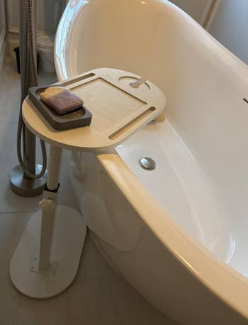 Freestanding bathtub with an adjustable tray holding soap, perfect  for a stylish bath  upgrade