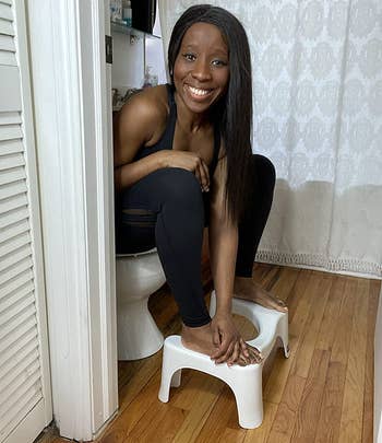 reviewer sitting on a toilet with their feet on the squatty potty