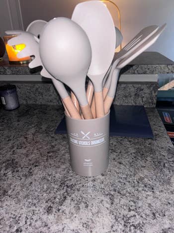 Set of room  utensils successful  a holder connected  a countertop, including spatulas and serving spoons