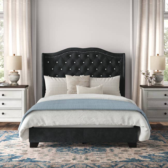 a black velvet bed frame with a tall upholstered and studded headboard