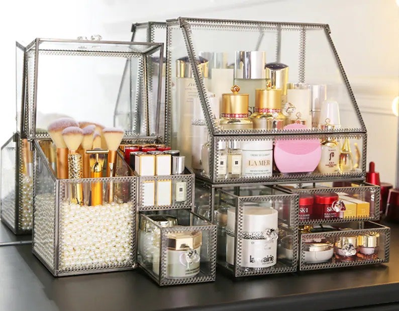 A glass makeup case set that is lined in a bronze-color copper material. It stores several makeup products and makeup tools