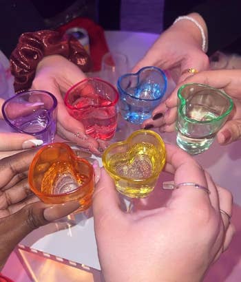 Seven hands clinking colorful heart-shaped shot glasses together