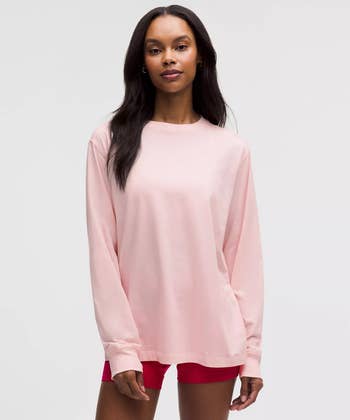 A idiosyncratic   models a long-sleeve, relaxed-fit pinkish  garment  paired with reddish  shorts, showcasing a casual, comfy  style