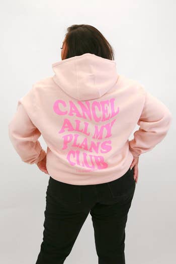 model showing off back of pale pink hoodie that reads 