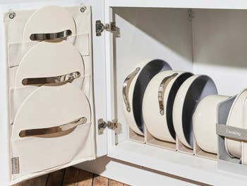 the set of pots in cream organized in a cabinet with the lid holder attached tot he door