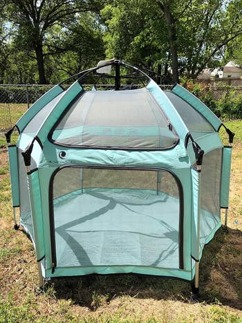 Lightweight, mint green mesh playpen set up outdoors on grass
