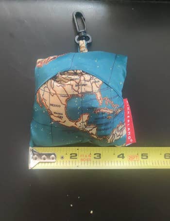 the laundry bag folded up into a tiny matching pouch next to a tape measure for scale