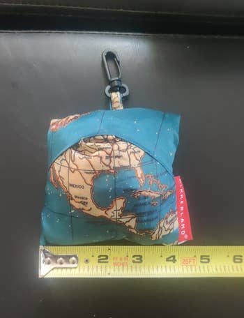 the laundry bag folded up into a tiny matching pouch next to a tape measure for scale