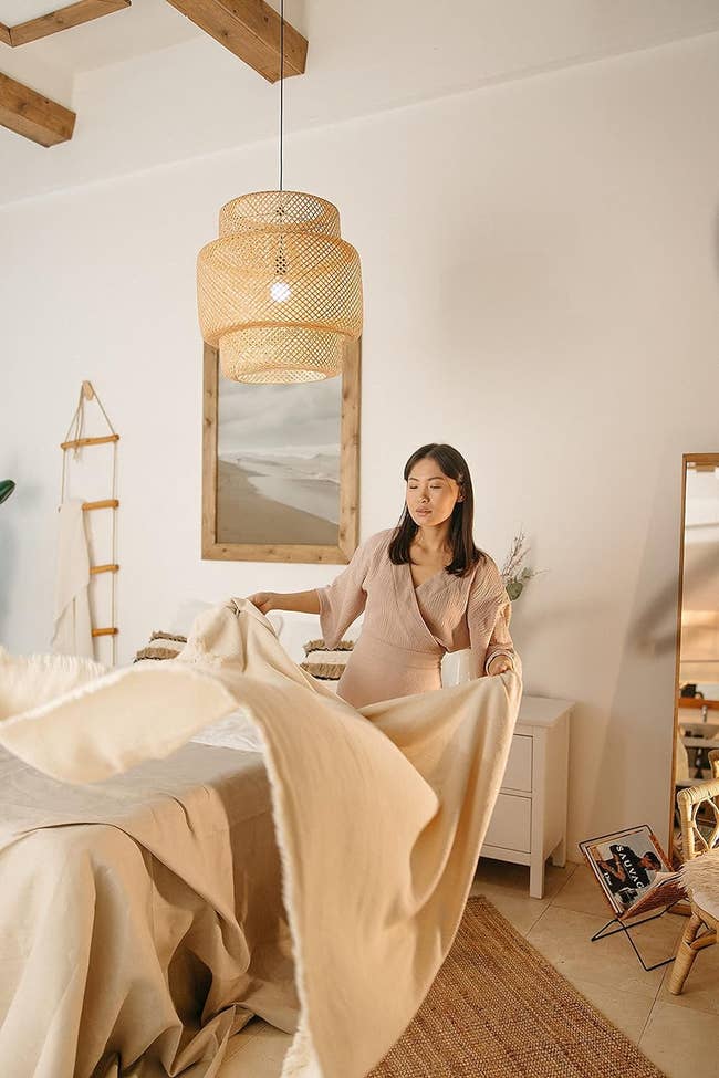 three tiered woven pendant light cover made with rattan. the image shows a person making their bed underneath the light.