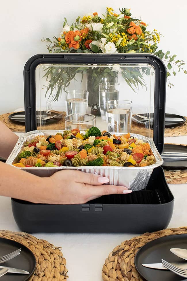 hand placing a foil pan of pasta salad into the black pan protector, which has tall and sturdy plastic sides