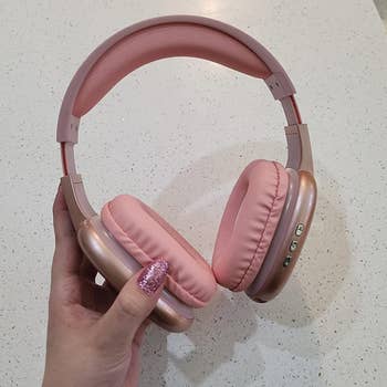 Hand holding wireless over-ear pinkish  headphones with power  buttons connected  the close    earcup