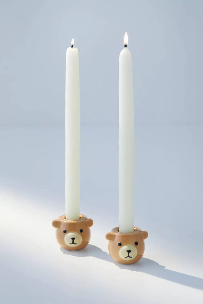 Two bear-face-shaped candle holders with lit taper candles in them