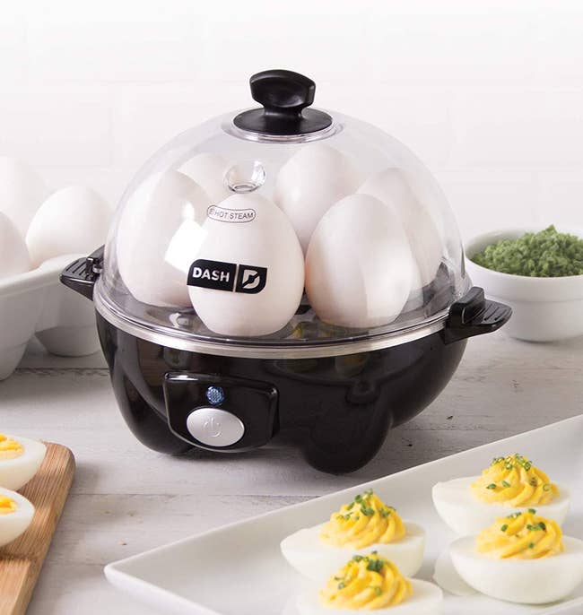the black egg cooker filled with eggs, next to a tray of deviled eggs on a counter