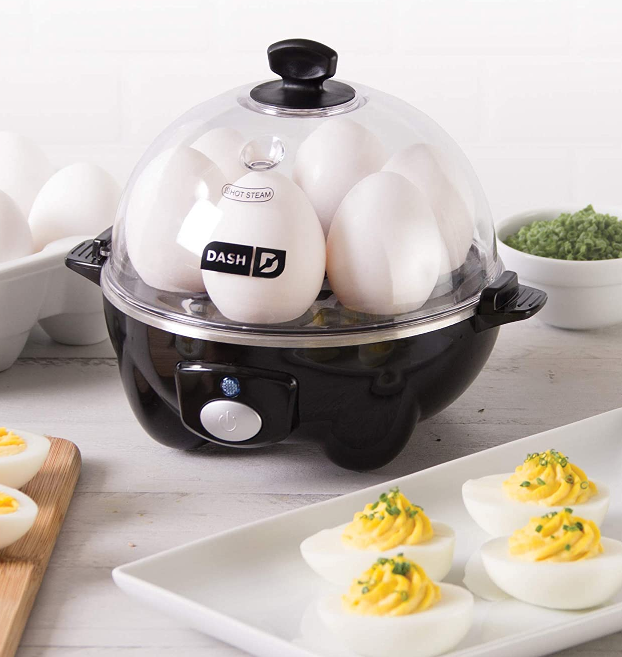 the black egg cooker filled with eggs, next to a tray of deviled eggs on a counter