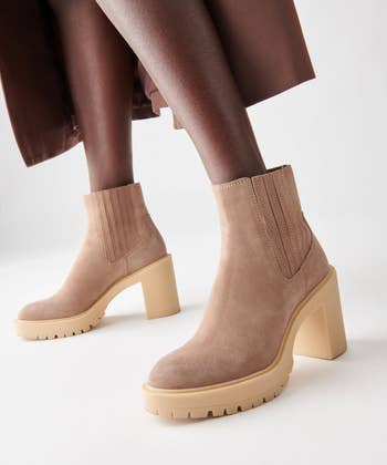 Person wearing tan suede ankle boots with chunky heels and ribbed side panels