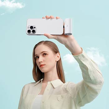 A model holding a phone with the white portable charger plugged in taking a selfie
