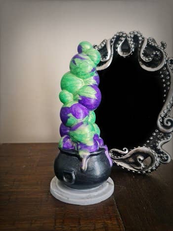 Green, purple and black boiling cauldron dildo in front of mirror