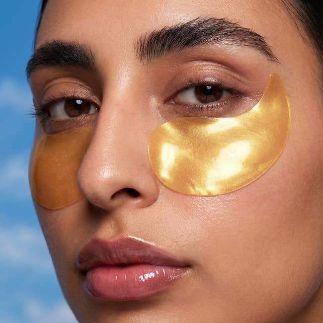 Person with golden under-eye patches for skincare treatment