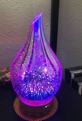 a reviewer's bulb shaped glass oil diffuser with purple and blue firework-esque lighting effects