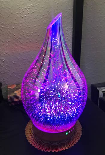 a reviewer's bulb shaped glass oil diffuser with purple and blue firework-esque lighting effects