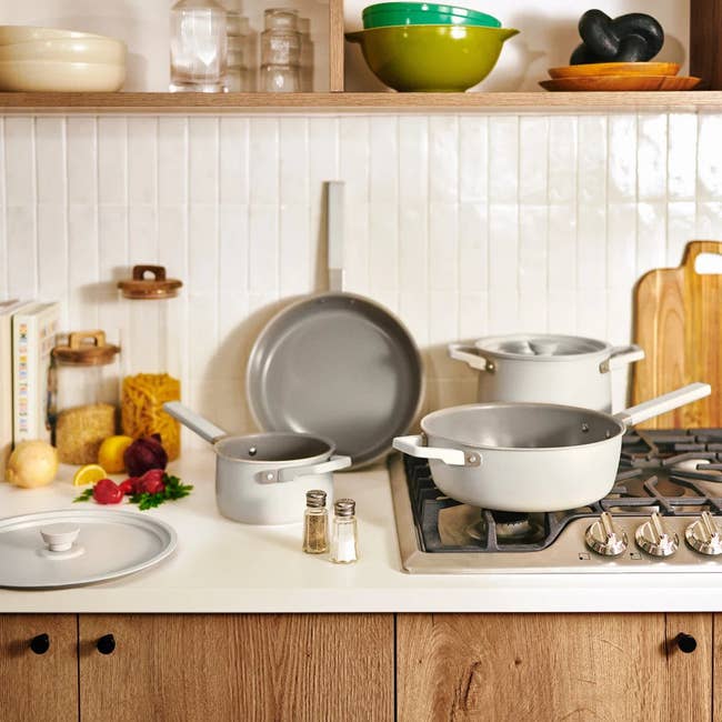 Modern kitchen with various cookware on the stove and counter, including pots and a pan. Wooden cabinets and accessories are visible in the background