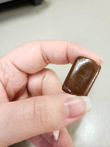 same reviewer holding an unwrapped brown rectangular candy