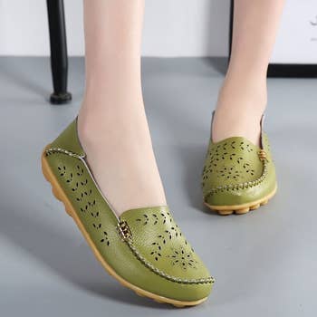 Model wearing same loafers in green with cut out flower pattern throughout
