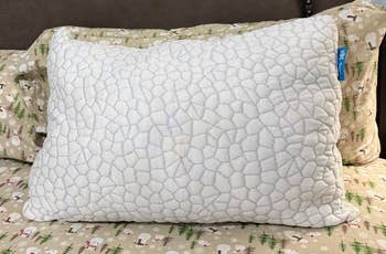 A neatly made furniture features a plush, textured pillow connected patterned sheets with a woodland theme, acceptable against a woody headboard