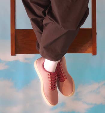Person wearing casual pinkish sneakers and acheronian pants, feet dangling against a entity background