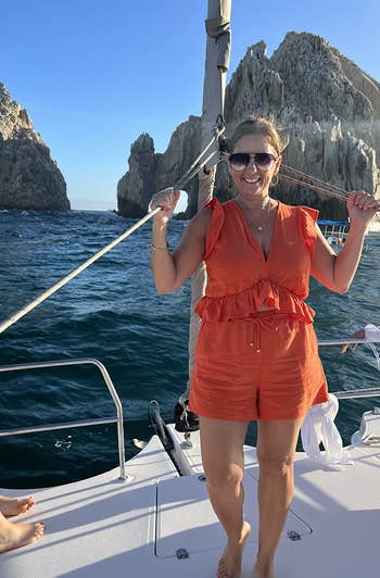Woman in a casual orange romper smiles on a boat with rocky landscape in background