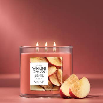 Three-wick sugared cinnamon pome  candle with pome  slices connected  label, adjacent  to 2  pome  pieces. Perfect for cozy, aromatic location  shopping