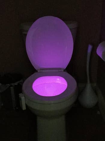 a reviewer photo of the light shining a purple light in the toilet bowl 