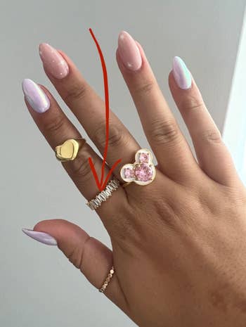 person wearing ring on index finger amongst other costumer jewelry rings