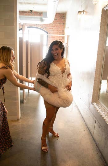bride in a bathroom with their skirt pulled up by a sheer white underskirt with arm holes 
