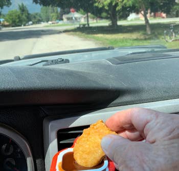 The dip clip clipped onto a reviewer's car air vent with sauce and reviewer dipping nugget in it