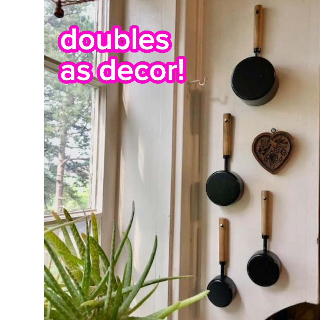 Four frying measuring cups with woody  handles are hung vertically connected  a wall; substance   reads 