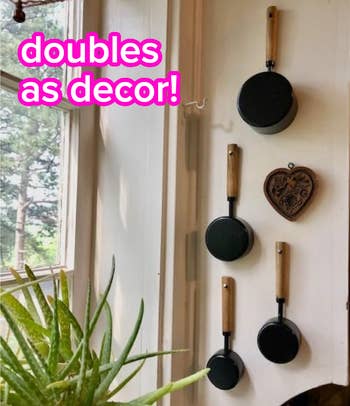 Four frying measuring cups with woody handles are hung vertically connected a wall; substance reads