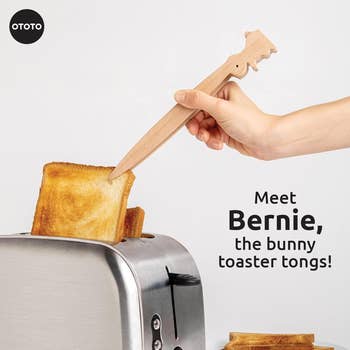 Hand using wooden bunny-shaped toaster tongs to remove toast from a toaster, product named Bernie by OTOTO