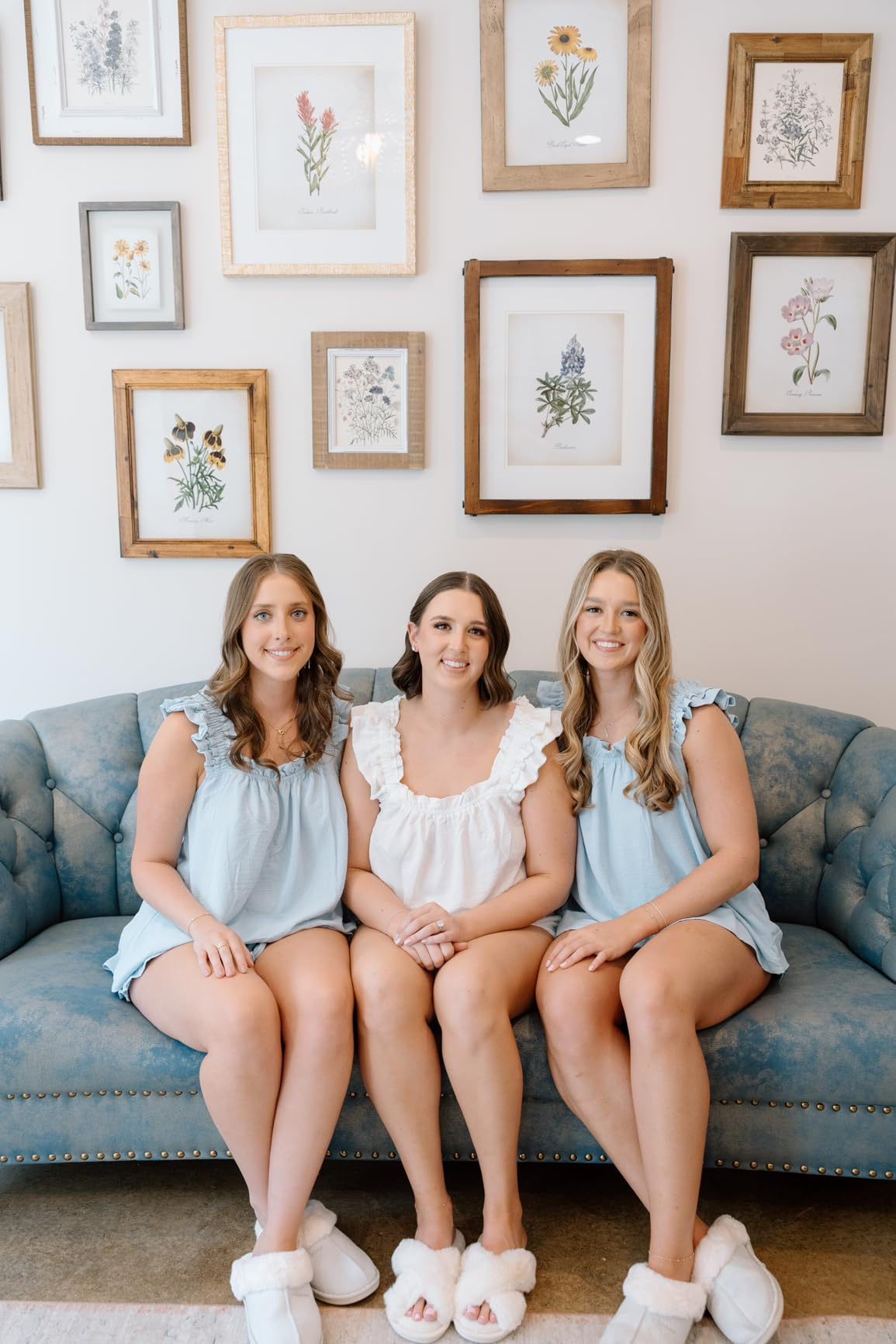 Three women seated connected  a bluish  couch, wearing matching ruffled tops and slippers. Botanical artwork is displayed connected  the partition  down  them