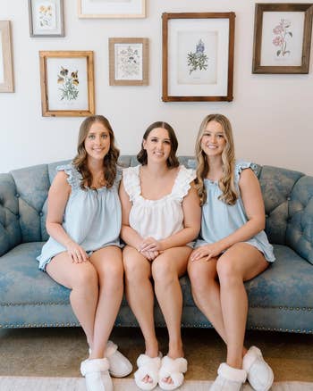 Three women seated connected a bluish couch, wearing matching ruffled tops and slippers. Botanical artwork is displayed connected the partition down them
