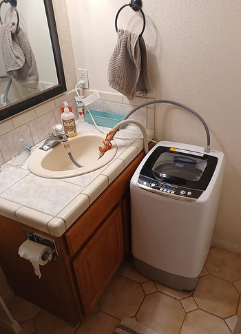 the small washer about as high as the bathroom counter hooked up to reviewer's sink