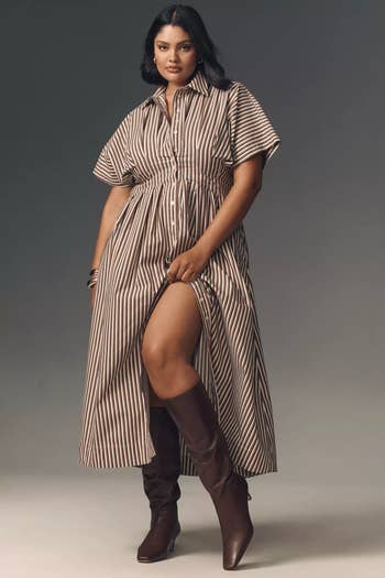 Person successful  a striped formal  with elbow-length sleeves and a beforehand   slit, paired with knee-high boots, stands confidently for a manner  buying  feature