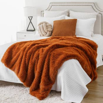 Bed with achromatic  linens, textured brownish  pillow, pick  knot pillow, and fluffy orangish  propulsion  broad  draped implicit    it. Modern decor style