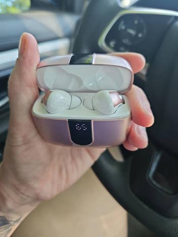 Person holding wireless earbuds with a charging case in a car interior