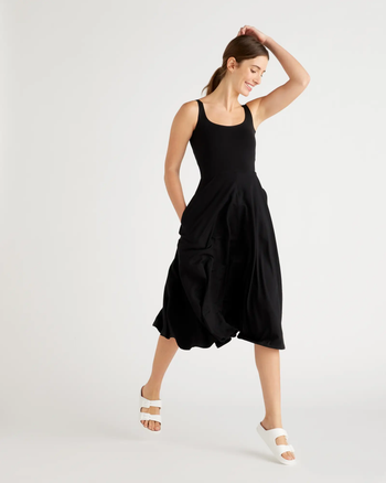 a model posing in a black midi tank top dress with white sandals