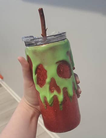 Reviewer holding a poison apple themed cup with a straw in it 
